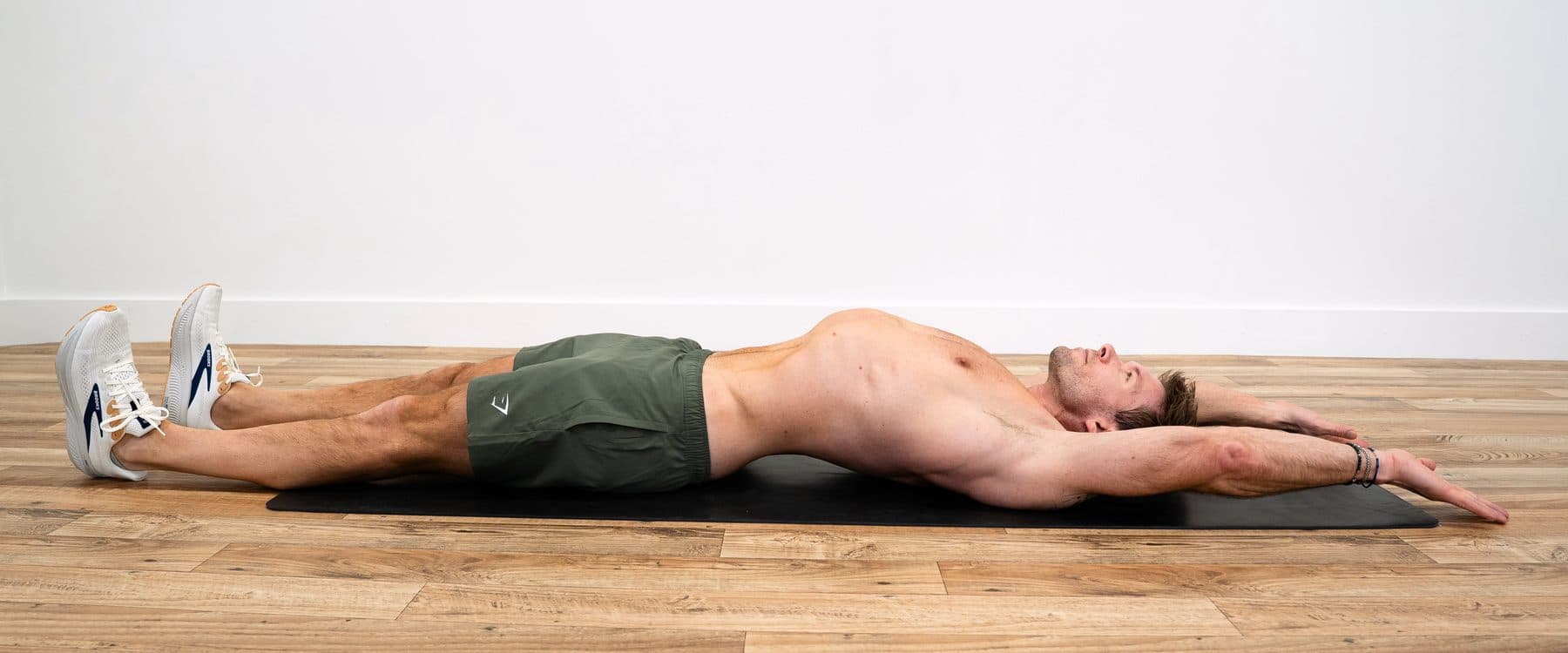Dan lying on his back on a mat, arms overhead and legs long, reaching in both directions